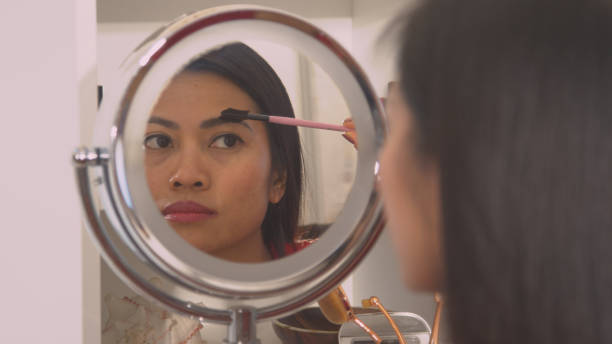 istock CLOSE UP: Young woman correcting eyebrow shape with brush in mirror reflection 1890695148
