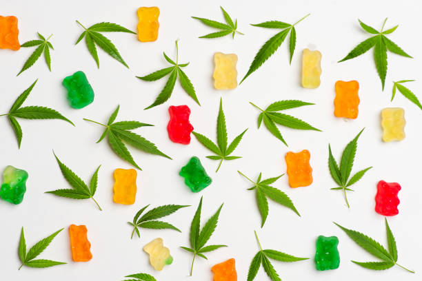 Cannabis gummy bears and cannabis leaves isolated on white pattern Pile of colorful gummy bears made with cannabis extract next to a hemp leaf. These medical marijuana edibles contain CBD and THC and are isolated on a white background cannabis gummy bears stock pictures, royalty-free photos & images