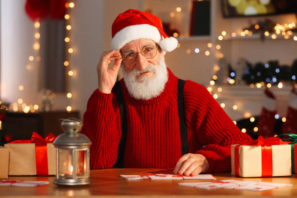 istock Santa Claus at his workplace. Letters and gift boxes on table in room with Christmas tree 1890757238