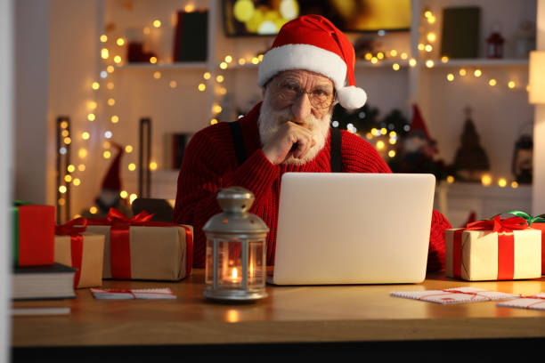 istock Santa Claus using laptop at his workplace in room decorated for Christmas 1890759285