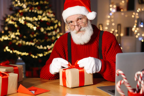 istock Santa Claus tying bow on gift box at his workplace in room decorated for Christmas 1890760321