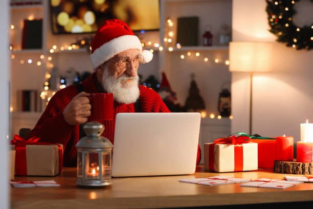 istock Santa Claus using laptop and drinking hot beverage at his workplace in room decorated for Christmas 1890761343