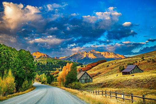 Two abandoned barns along a hillside with the peaks of Rocky Mountains in the distance shot on fall morning at daybreak near Telluride, Colorado.