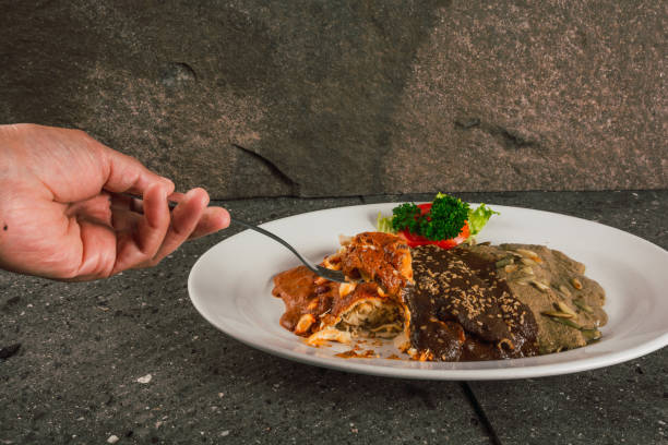 Woman hand cutting enmoladas de encacahuatado, mole negro, pipian served on the same white plate, stuffed with chicken.