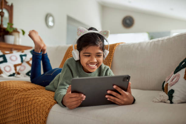 istock Little Girl Using Tablet At Home Lying On Sofa With Headphones 1890895118