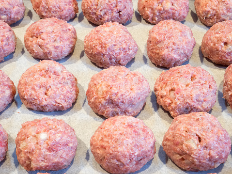 Delectable meatballs, neatly arranged on a baking tray lined with parchment paper, poised for their initial oven bake preceding the frying process.