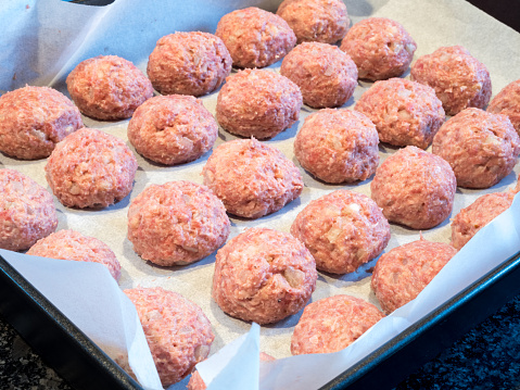 Delectable meatballs, neatly arranged on a baking tray lined with parchment paper, poised for their initial oven bake preceding the frying process.