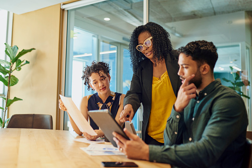 A multiethnic group of business professionals having a meeting in a modern office space. They are discussing a project while looking at a tablet.