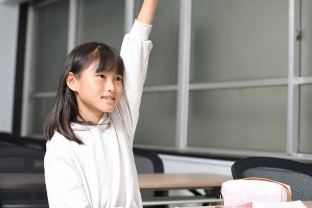 asiatisches grundschulmädchen hebt ihre hand während des unterrichts im klassenzimmer - elementary student classroom education elementary school building stock-fotos und bilder
