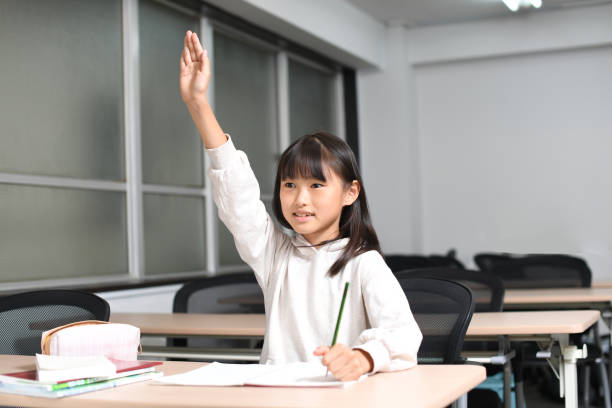 asiatisches grundschulmädchen hebt ihre hand während des unterrichts im klassenzimmer - elementary student classroom education elementary school building stock-fotos und bilder