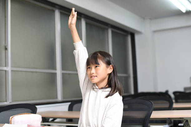 asiatisches grundschulmädchen hebt ihre hand während des unterrichts im klassenzimmer - elementary student classroom education elementary school building stock-fotos und bilder