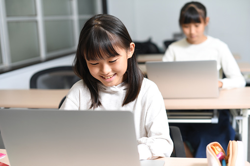 Several Asian elementary school girls participate in class using laptops in the classroom.