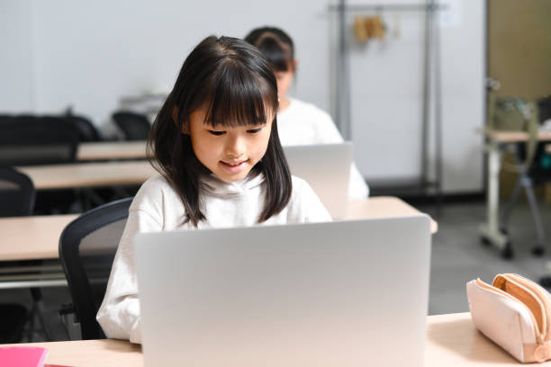Several Asian elementary school girls participate in class using laptops in the classroom.