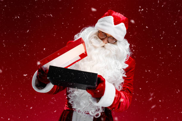 istock Santa Claus holding and opening gift box looking inside isolated on red background 1891070589