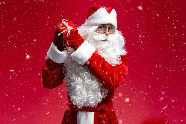 istock Santa Claus holding gift box looking at camera isolated on red background. winter concept 1891071100