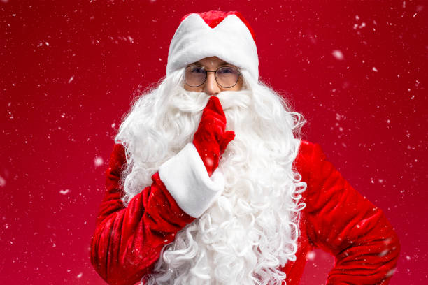 istock Santa Claus holding finger on lips looking at camera isolated on red background 1891072156