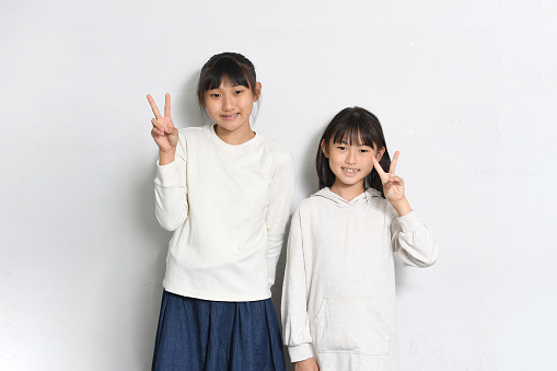 Asian elementary school girl smiling and looking at the camera and making a peace sign in front of a white background