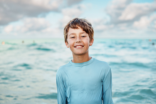 A portrait of a smiling elementary school aged boy of Caucasian descent standing in the ocean.