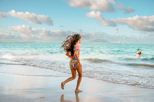 Rear view of an elementary school aged girl of Caucasian descent running into the shallow ocean during a weekend trip to the beach in Hawaii.