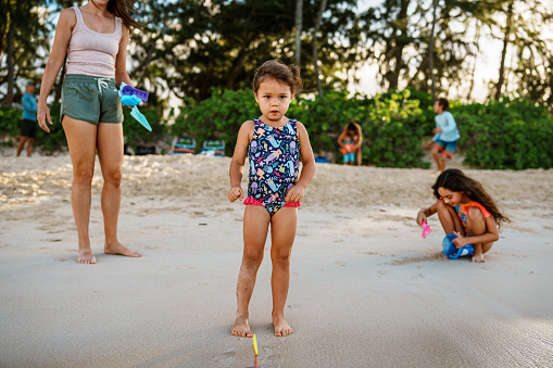 A cute Eurasian three year old girl has fun playing with her cousins at the beach while on a multi family vacation in Hawaii.