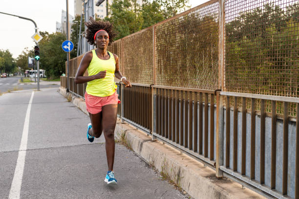 Athletic mature woman running on street in city during sunset.