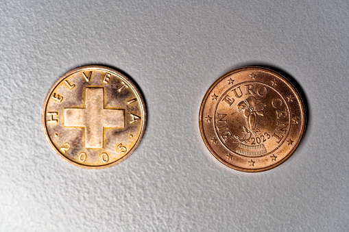 Close-up of two copper coins value one Rappen and one Euro Cent against gray background. Photo taken December 28th, 2023, Zurich, Switzerland.