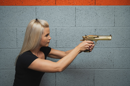 A blonde girl takes aim from a golden Desert Eagle pistol. Side view. Close up photo