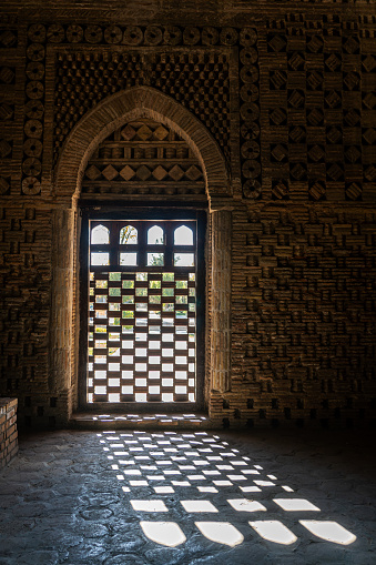 a lattice window letting in the bright light of the sun inside the Samanid mausoleum in Bukhara, Uzbekistan.
