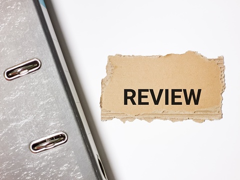Review written on brown paper strip with ring file against white background.