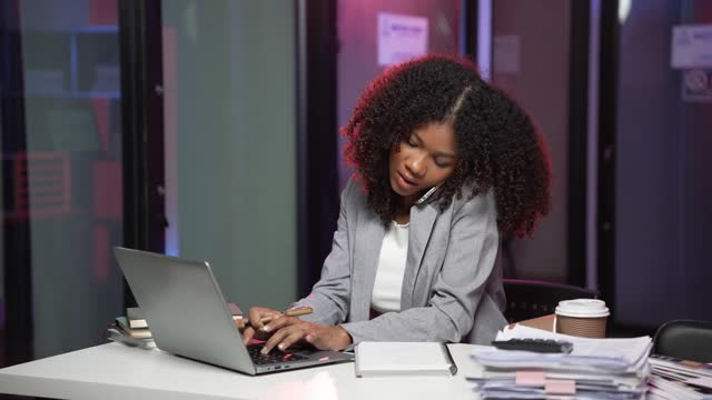 Beautiful African woman in business suit talking on mobile phone while working at table in office using modern smartphone to talk with client for consultation 4k 60p