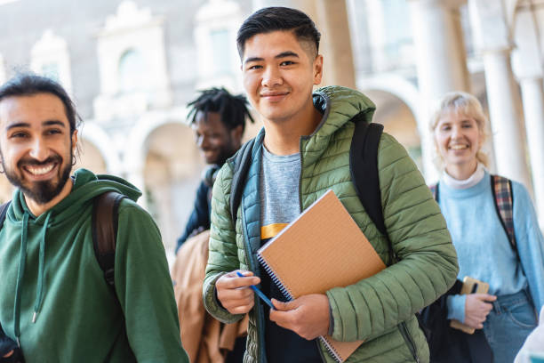 Smiling Students Enjoying Campus Life Cheerful diverse students with books and backpacks share a joyful moment, embodying friendship and diversity. male chinese student stock pictures, royalty-free photos & images