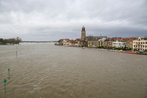 Deventer at the river IJssel with high water level after heavy rainfall upstream in Germany in December 2023. People are looking at the river and the temporary sand bag barrier on the quay.