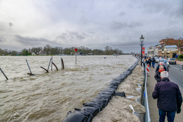 Deventer at the river IJssel with high water level after heavy rainfall upstream in Germany in December 2023. People are looking at the river and the temporary sand bag barrier on the quay.