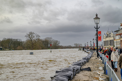Deventer at the river IJssel with high water level after heavy rainfall upstream in Germany in December 2023. People are looking at the river and the temporary sand bag barrier on the quay.