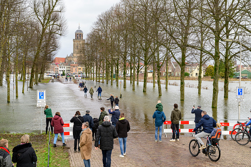 Deventer at the river IJssel with high water level after heavy rainfall upstream in Germany in December 2023. The park and parkinglot at the Worp is flooded, but people are still crossing the road towards the ferry to the city.