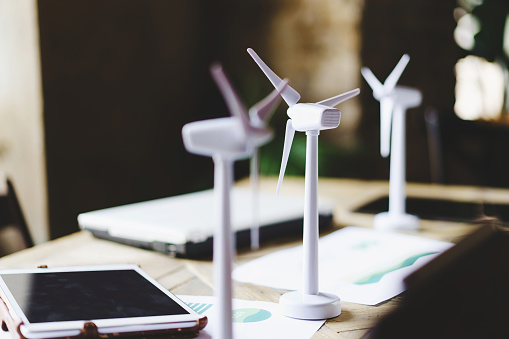 Close up of wind turbines on a table desk with data sheets, tablet and laptop computer plan blueprints. Green ecology, renewable energy and eco sustainability lifestyle architecture - no people