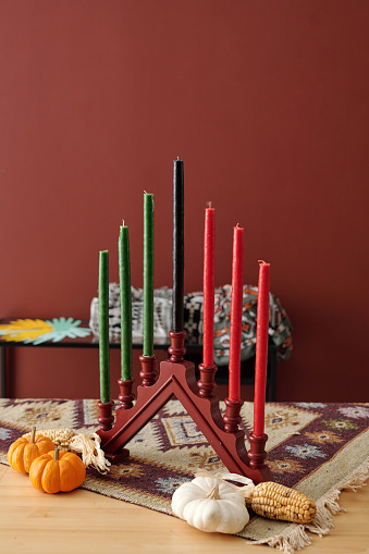 Candlestick with seven multi-colored candles and ripe vegetables standing on table in front of camera before celebration of Kwanzaa