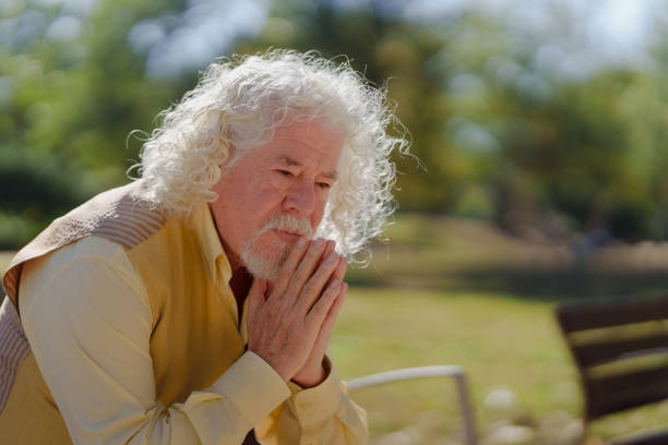 Close up of senior man (80s) with eyes closed and hands clasped.
