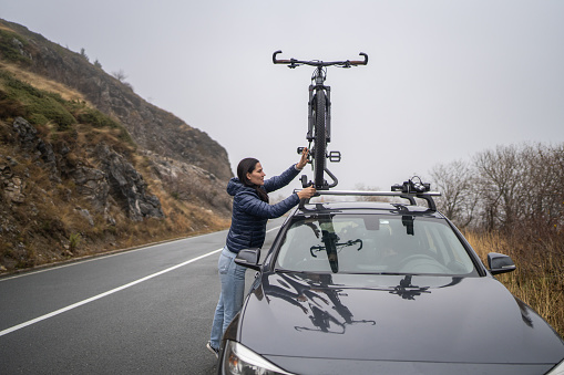 Woman mountain biker takes of her bike from the car roof on the road.