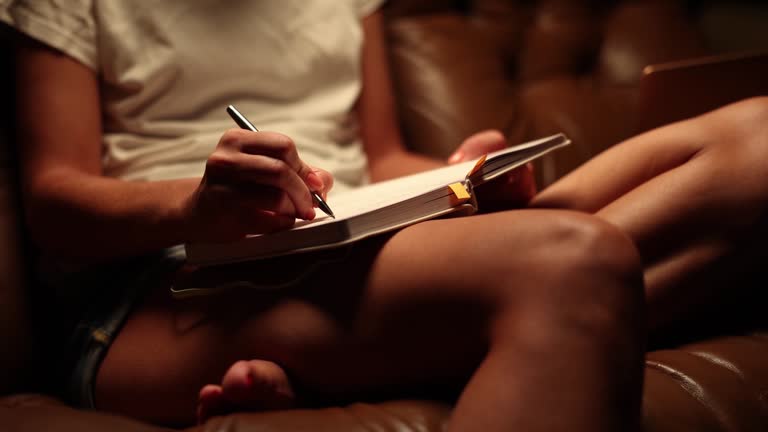 Woman is sitting on couch writing notes or planning tomorrow evening