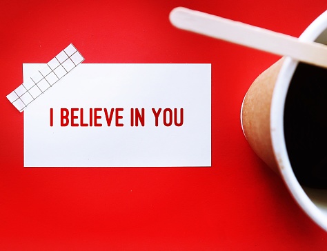 On red background, coffee cup and note with handwritten text I Believe in You - concept of supportive message to encourage love one or positive affirmation to boost self love, respect and self esteem