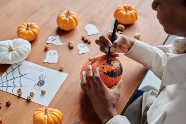 istock Young unrecognizable woman drawing scary face on orange pumpkin 1891741802