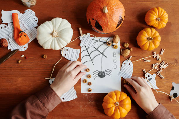 istock Hands of unrecognizable girl putting tiny decorations on Halloween postcard 1891741809