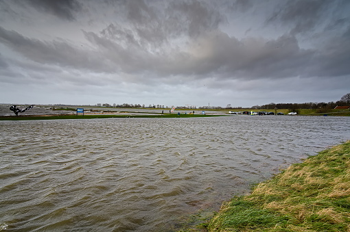 Lake floods the beach with kite surfers, parking lot with cars and the meadows outside the dike due to high water and strong gusts of wind with rain. Schellinkhout, Markermeer, Netherlands