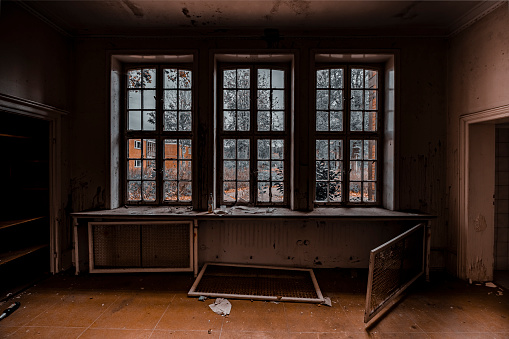 Abandoned school building interior with damaged floors and ceilings. Light is coming in through the dirty and damaged windows.