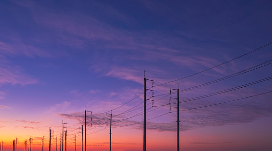 Silhouette two rows of electric poles with cable lines against colorful dramatic twilight sky background, low angle view with copy space