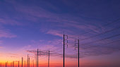 Silhouette two rows of electric poles with cable lines against colorful dramatic twilight sky background