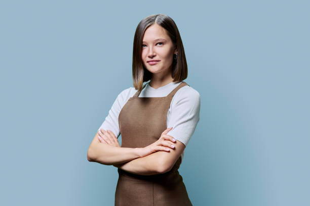 istock Young smiling woman in apron looking at camera on blue studio background 1891817172