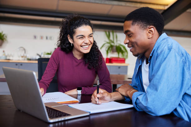 College students smiling while working on a laptop in a campus lounge