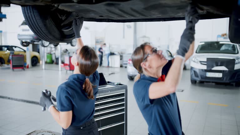 SLO MO A team of women mechanics working together at the repair shop. Female maintenance engineers working under car in repair shop